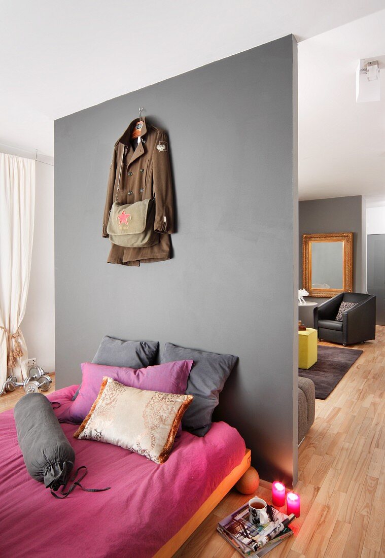 Französisches Bett mit pink-grauen Textilien vor einer Raumteilerwand zum Wohnbereich