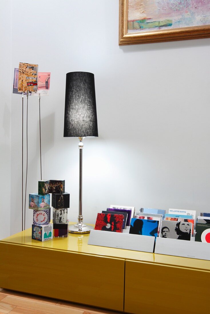 Collection of CDs, cube ornaments and table lamp on low sideboard