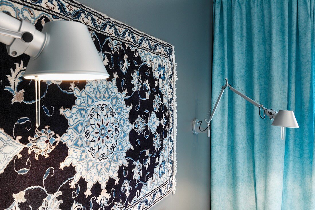 Silk rug on bedroom wall flanked by Tolomeo lamps with pastel blue curtain in background