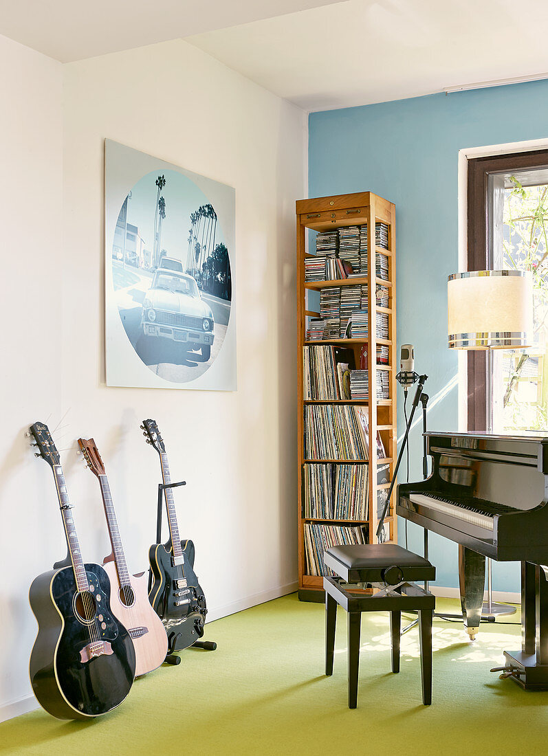 Verschiedene Musikinstrumente vor schmalem, hohem Holzregal in Zimmerecke, an hellblau getönter Wand