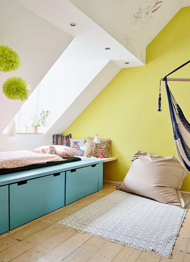 Minimalist bed below skylight and beanbag against yellow-painted gable-end wall in teenager's bedroom