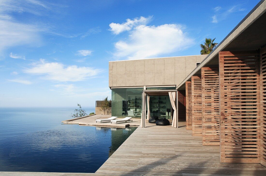 Contemporary house with open wooden louvre doors, encircling terrace and infinity pool with sea view