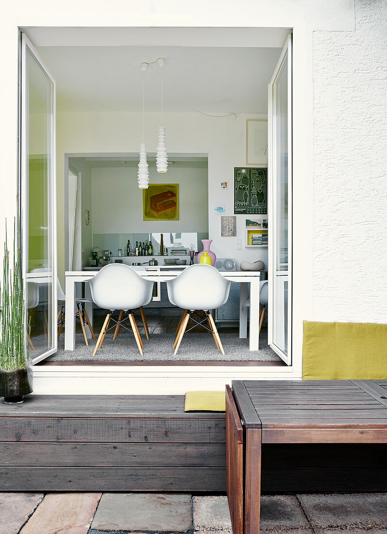 View from terrace through open double doors into dining room with classic chairs around modern table