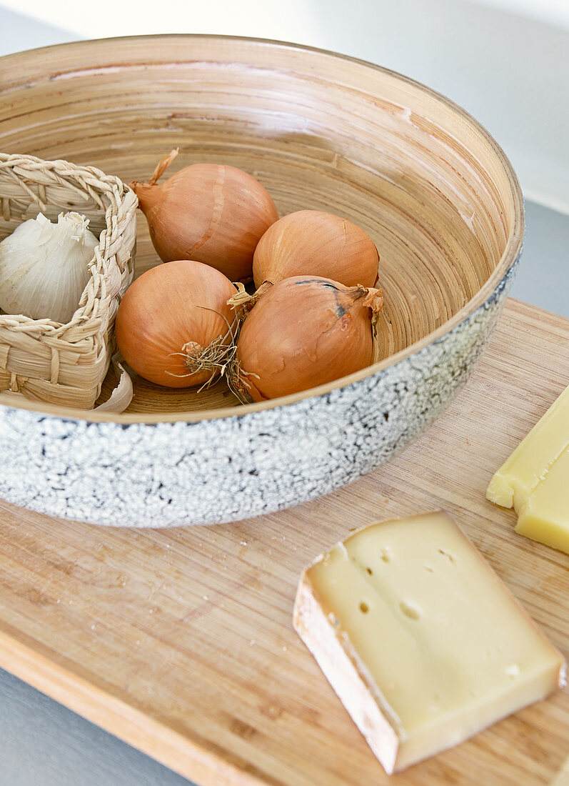 Schale mit Zwiebeln und Knoblauch neben Käse auf Holzbrett