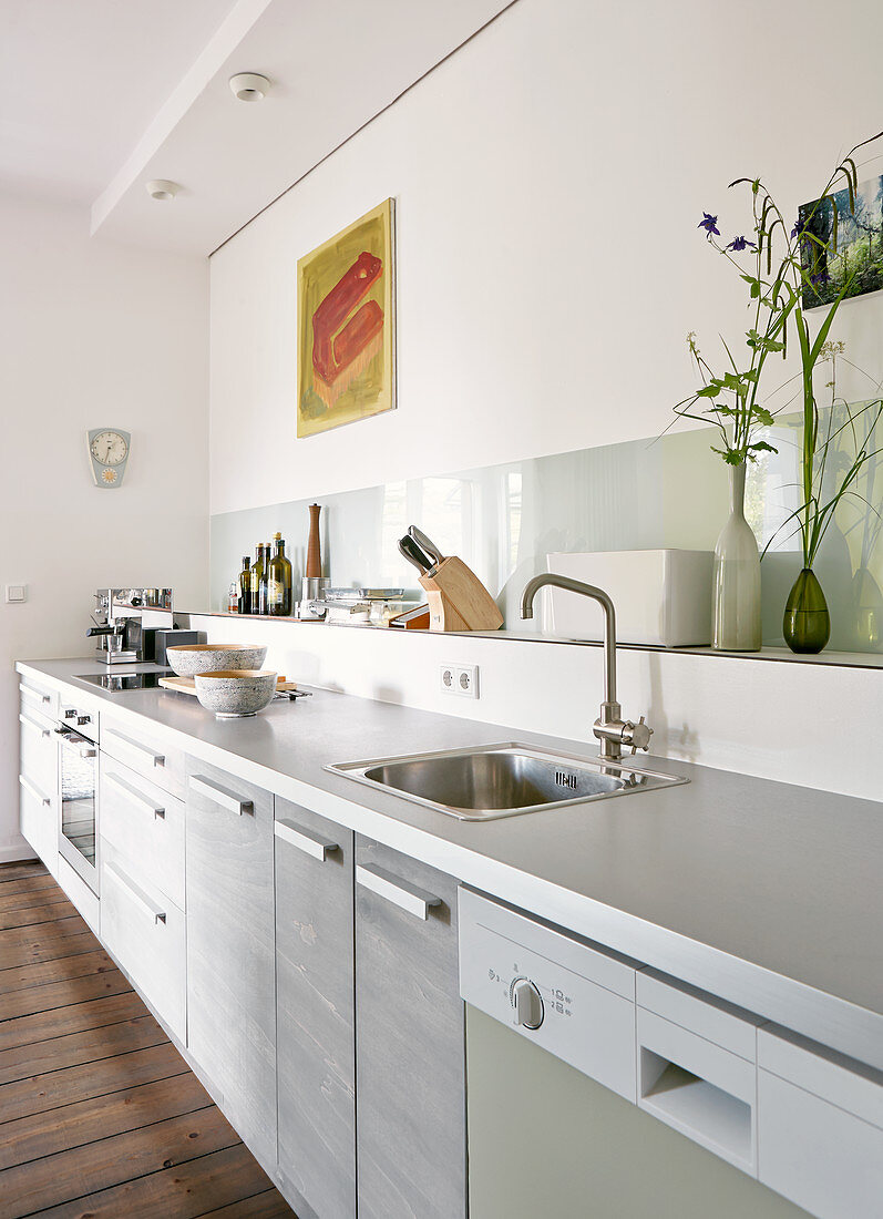 Moderne Küchenzeile mit hellgrauer Arbeitsplatte, Ablage vor Wand mit Küchenutensilien