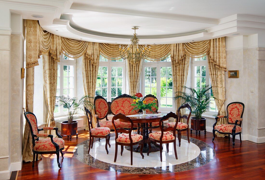 Halbkreisförmiger Erker mit Sitzplatz aus Stilmöbel, Stühle mit rotgoldenem Ornamentmuster vor Sprossenfenster mit Schabracken, in herrschaftlichem Ambiente
