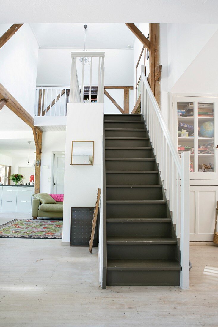Dark wooden staircase with white balustrade in open-plan interior; view into kitchen to one side
