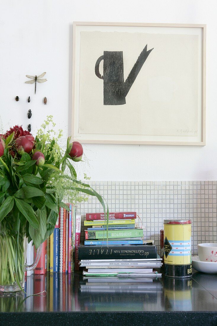 Bücherstapel auf Ablage, vor teilweise gefliester Wand, darüber Bild mit minimalistischem Motiv