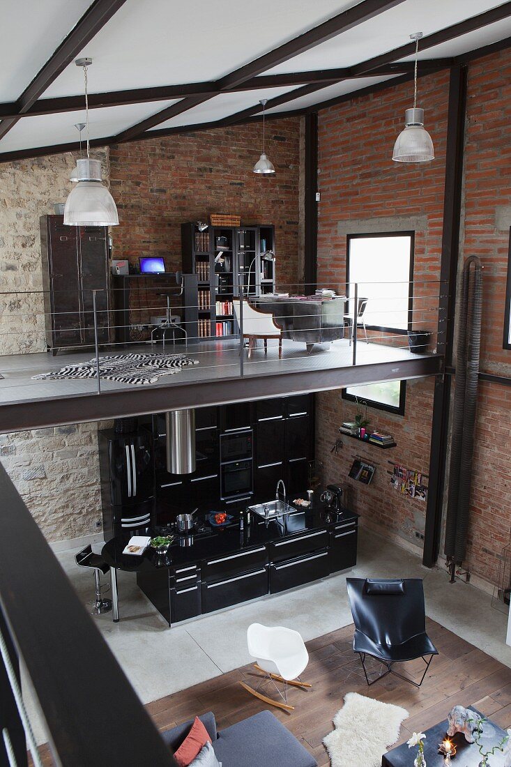 Blick von Galerie in Loft Wohnraum mit Klassiker Sitzmöbel und offener schwarzer Designerküche