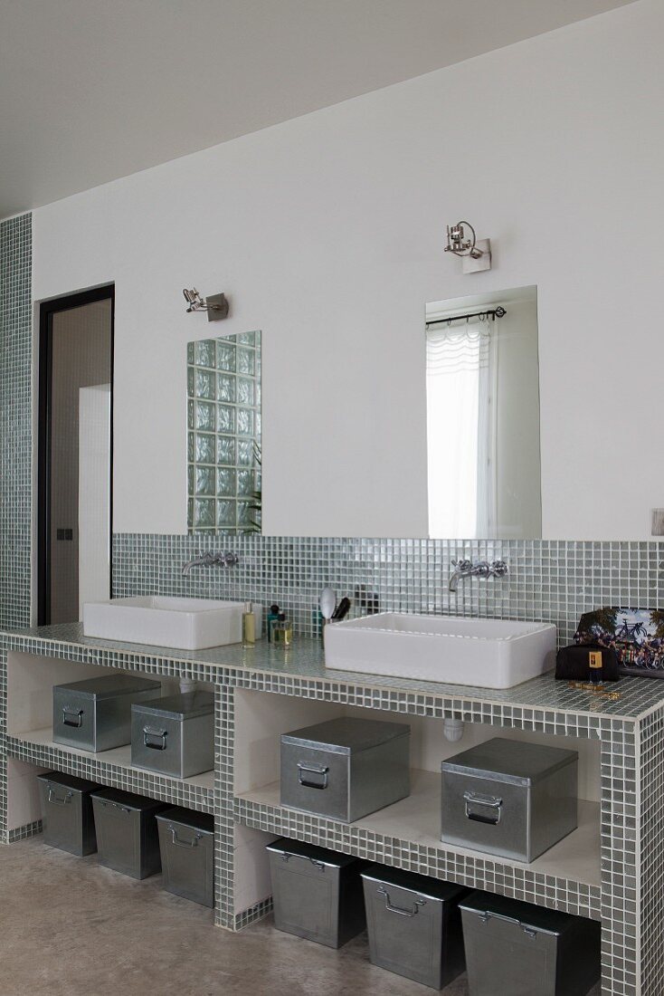 Masonry washstand covered in shiny silver mosaic tiles with twin countertop sinks in modern bathroom