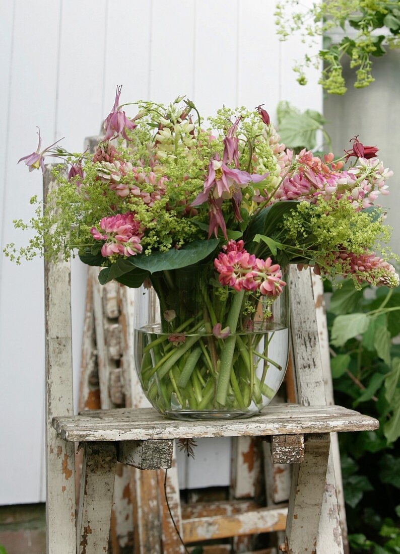 Glass vase of pink lupins on weathered wooden chair