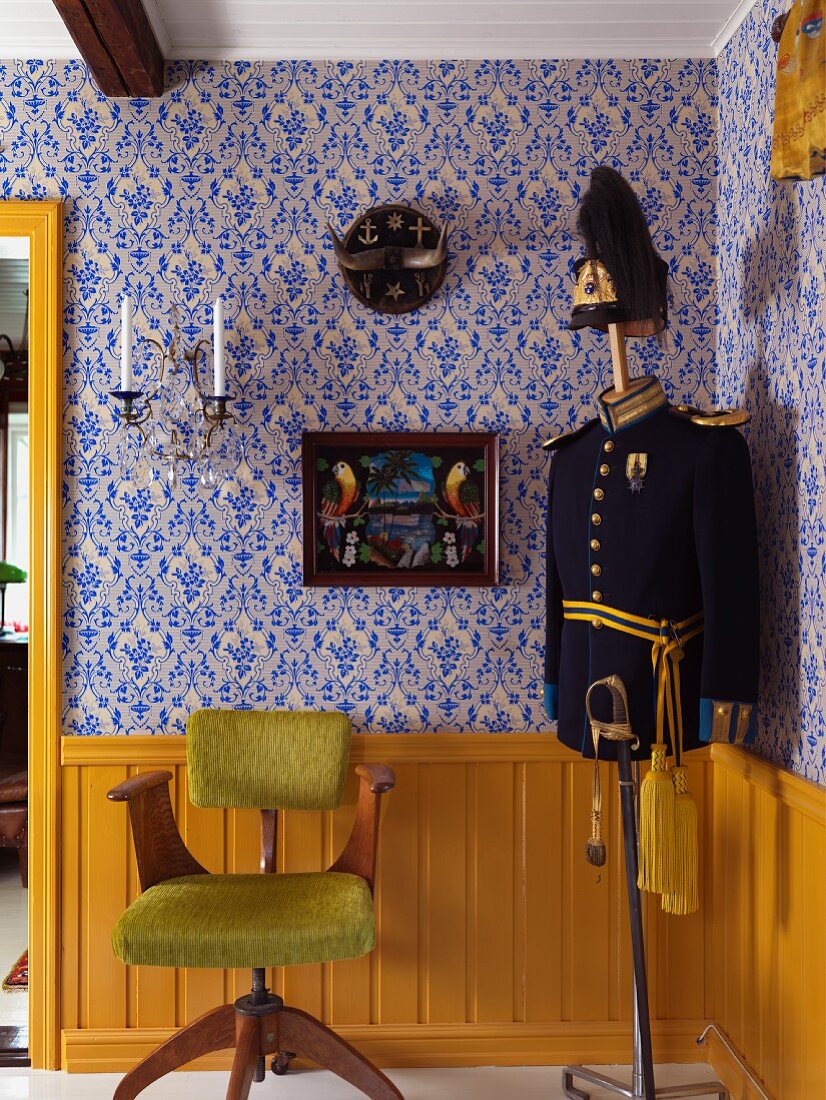 Holz Drehstuhl mit lindgrünem Fellbezug und Schneiderpuppe mit alter Uniform, vor gelb lackierter Brüstungswand, darüber tapezierte Wand mit Ornamentmuster