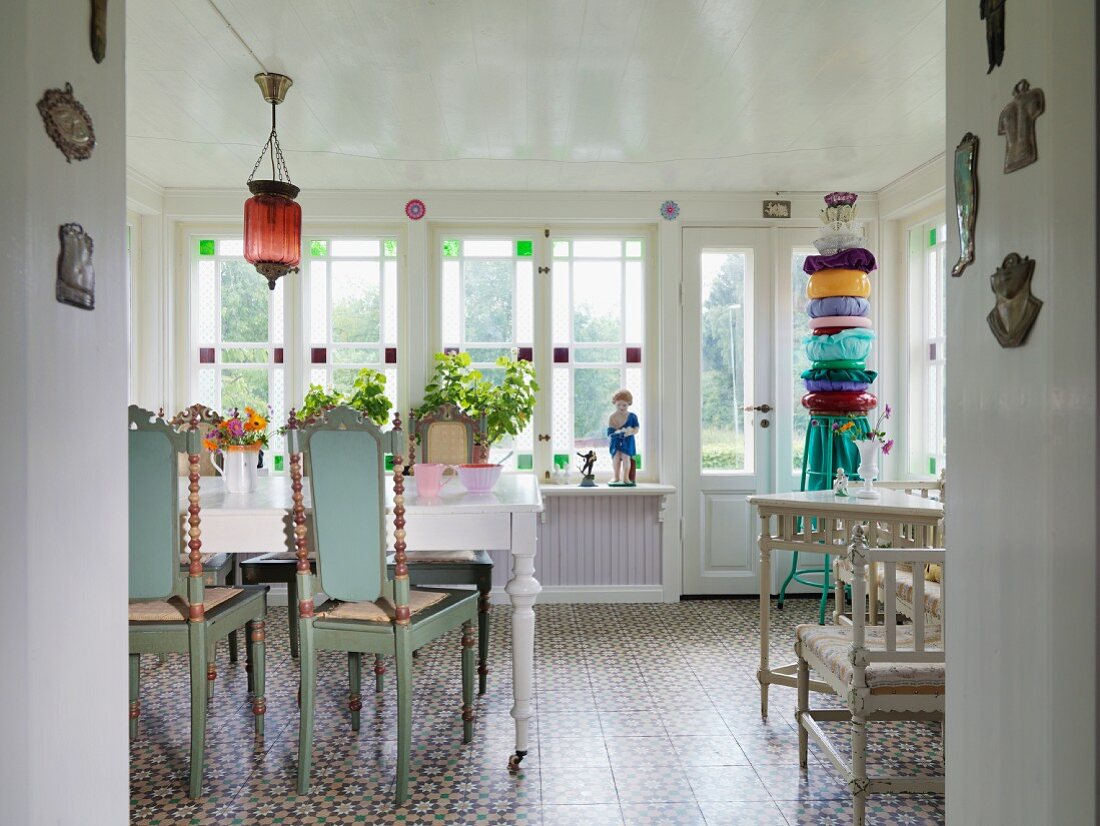Holzstühle mit geschnitzter Rückenlehne türkisfarben lackiert vor weißem Esstisch, im Hintergrund Fenster mit farbigen Glasfüllungen, in ländlichem Esszimmer