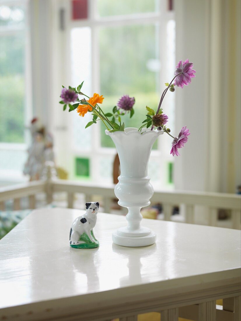 Gartenblumen in weisser Retro Porzellanvase und Porzellan Tierfigur auf Tisch