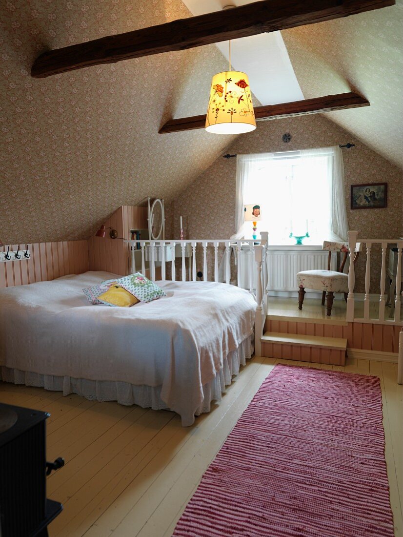 Schlafzimmer unter dem Dach, Doppelbett mit weisser Tagesdecke vor Empore mit weisser Holzbalustrade