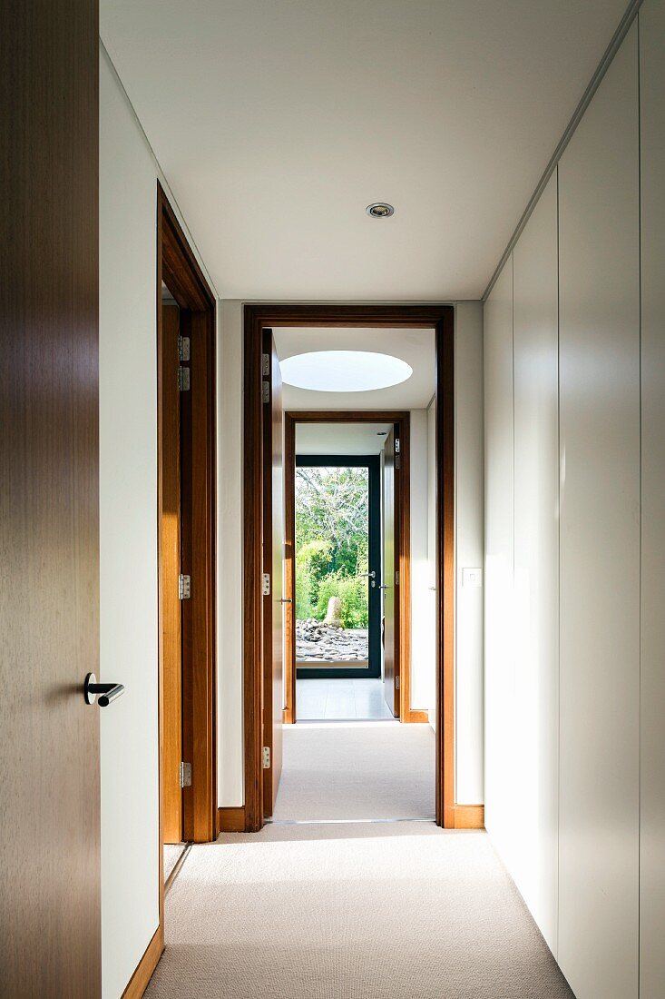 Narrow corridor with wooden interior doors, round skylight and white, fitted cupboards along one side