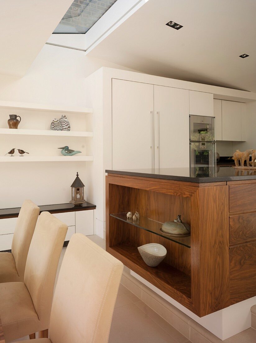 Gepolsterte Esszimmerstühle vor Küchenblock aus Massivholz und weiße Einbauschränke in offener Küche
