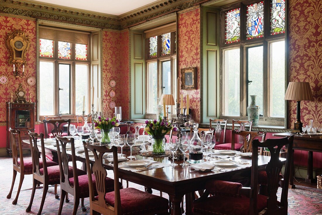 Festively set table in grand dining room with red and gold patterned wallpaper and wood-panelled window reveals