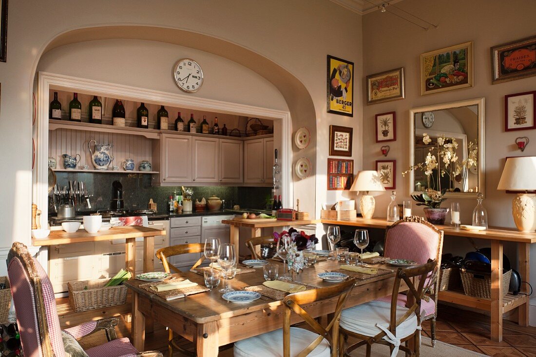 In Nische integrierte Küchenschränke und Wände in pastellrosa, vorne gepolsterte Armlehnstühle, Camargue Stühle und gedeckter Tisch aus alter Eiche