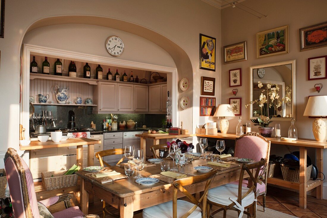 Kitchen cabinets integrated in niche, pastel pink walls, upholstered armchairs, Camargue chairs and place settings on old oak table