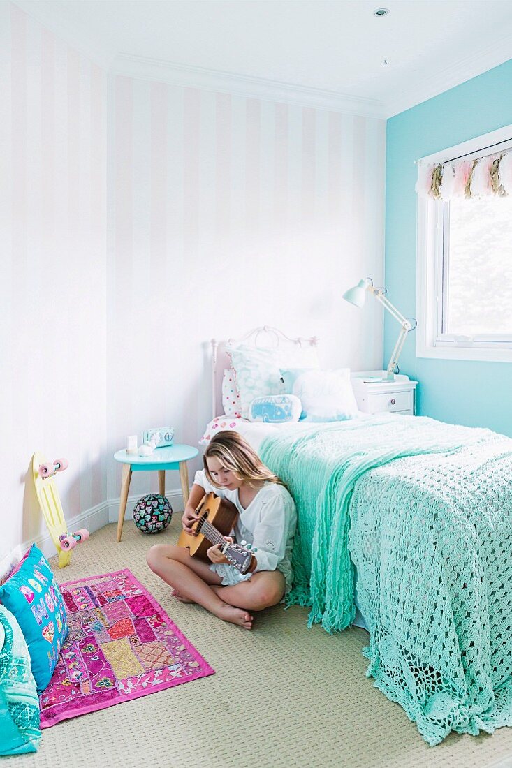 Mädchen spielt im pastellfarbenen Kinderzimmer Gitarre, Bett mit minzfarbener Häkeldecke