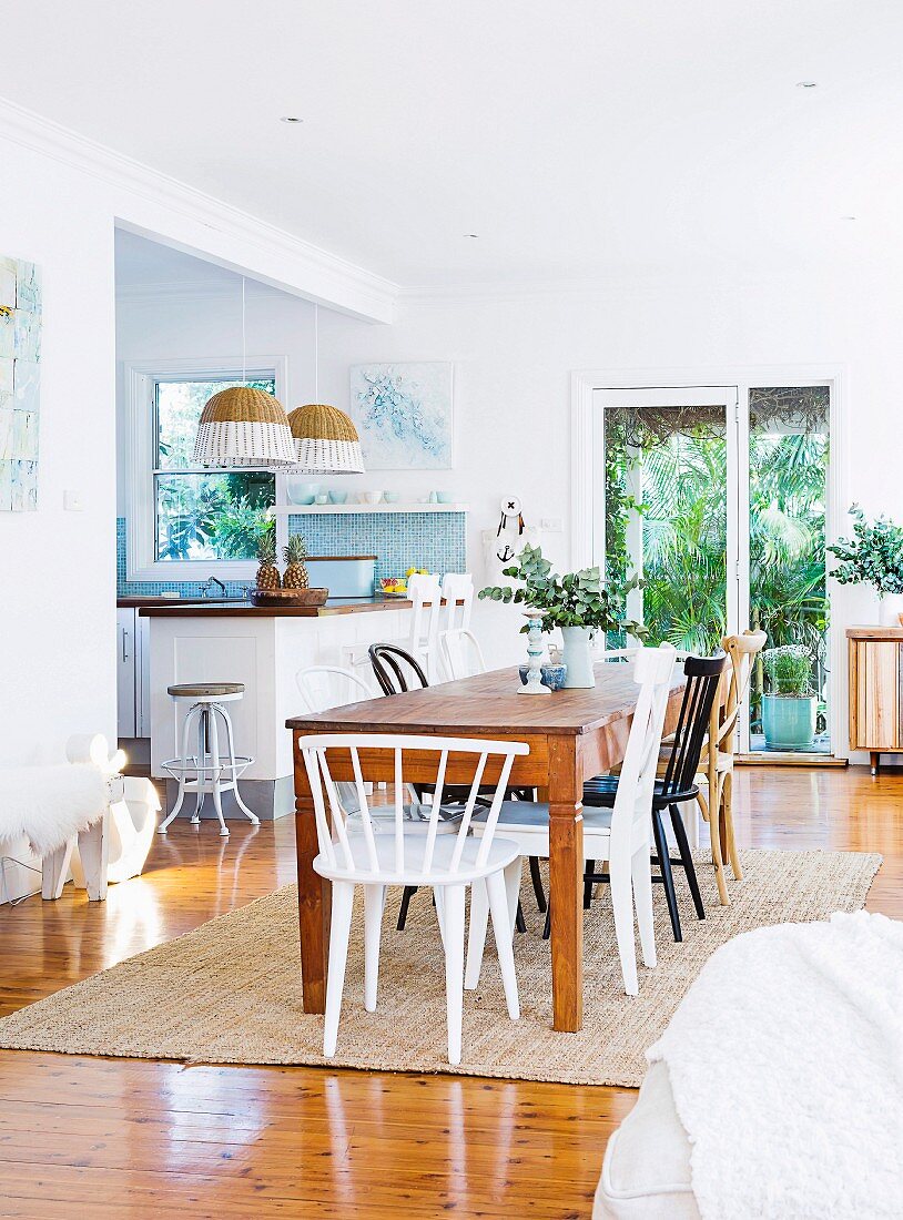 Wooden table, various chairs and view into kitchen in open-plan dining area