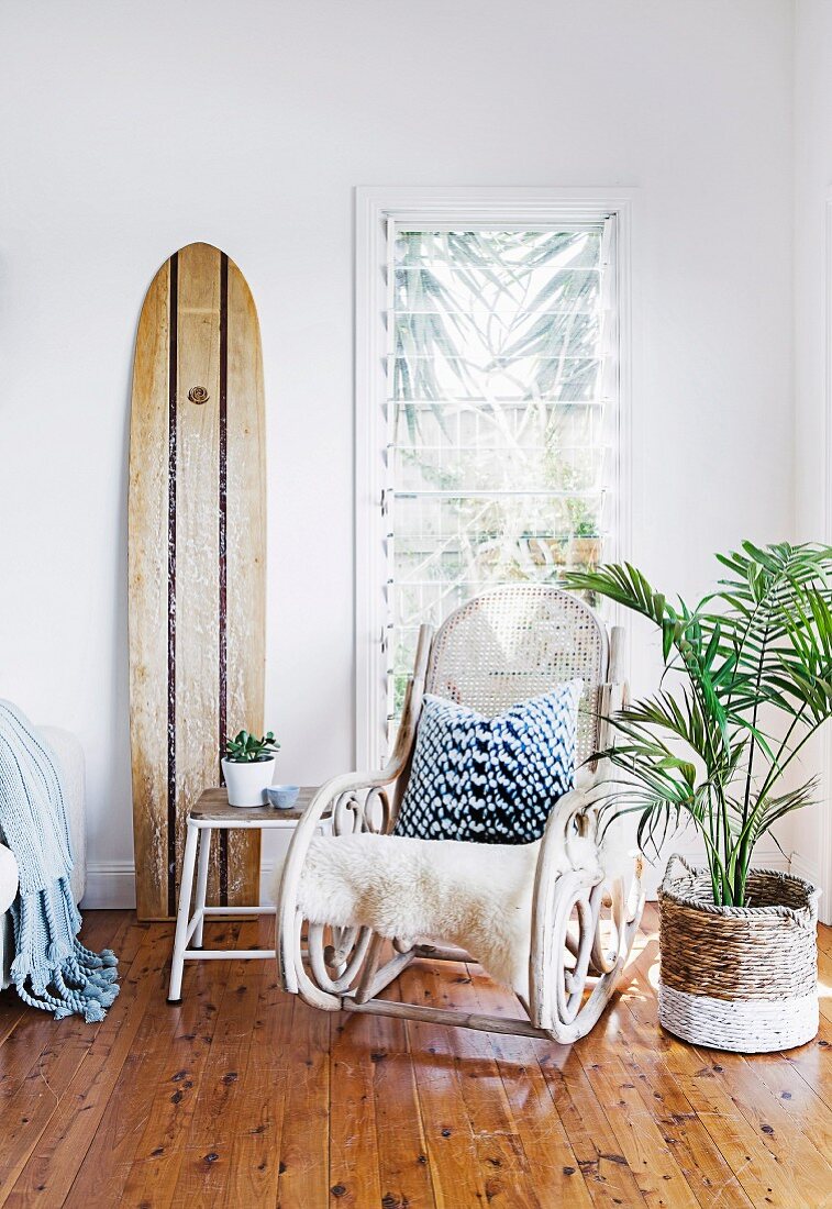 Rocking chair, surfboard and house plant in paint-dipped basket in exotic seating area
