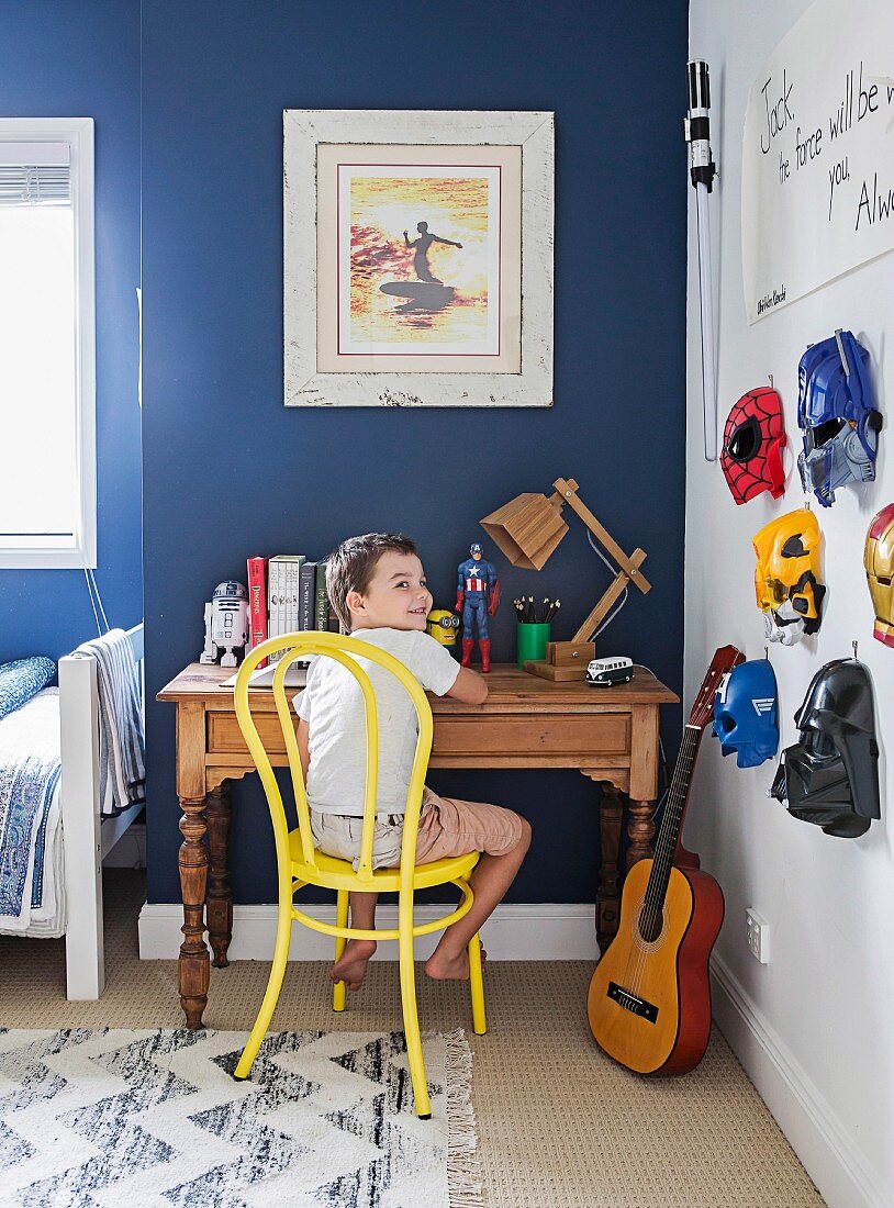 Junge sitzt im Kinderzimmer am Schreibtisch, an der Wand hängen Superheldenmasken