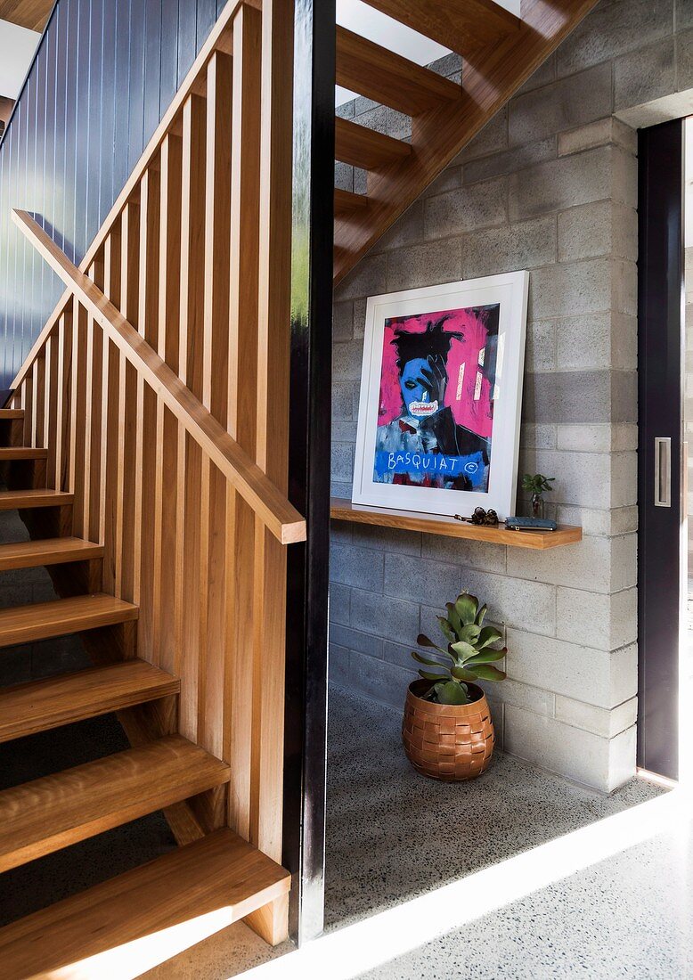 Dog-leg stairs with wooden slatted side wall and modern artwork on grey concrete-block wall of hallway