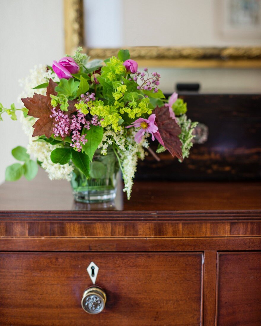 Glass vase of garden flowers on wooden chest of drawers