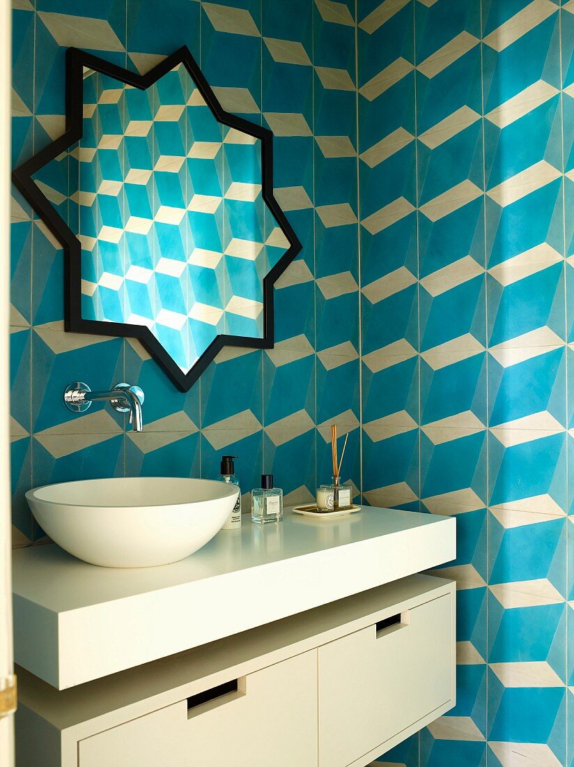 Moderner Waschtisch mit aufgesetzter Schüssel und sternenförmiger Spiegel, an gefliester Wand mit blau-weißem, dreidimensionalem Muster