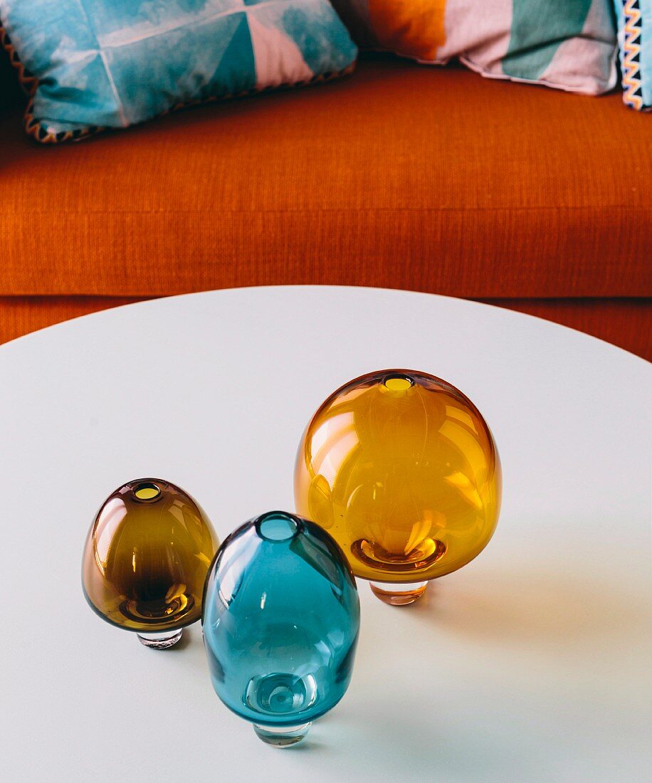 Retro vases made of brown and blue smoked glass on a white coffee table in front of an orange sofa