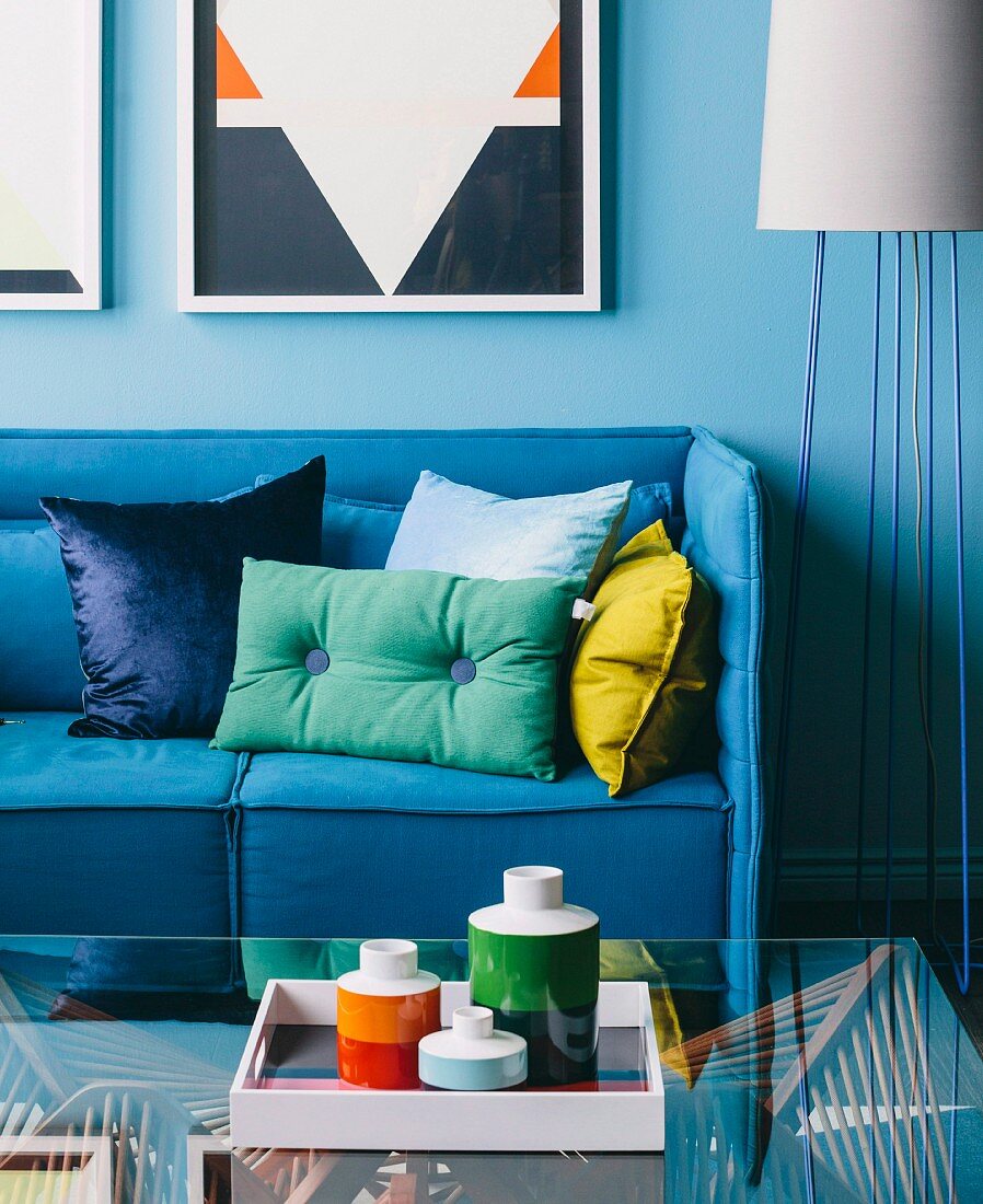 Blue couch with pillows and tray with retro vases on glass table