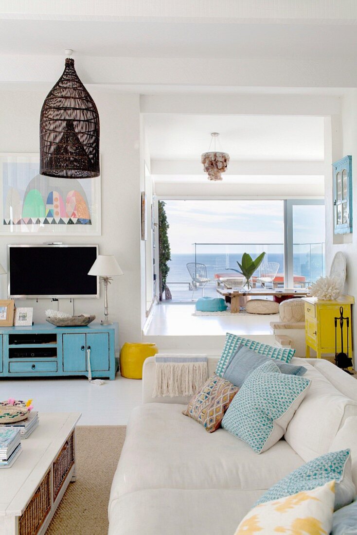 White couch with turquoise patterned cushions in bright interior with sea view