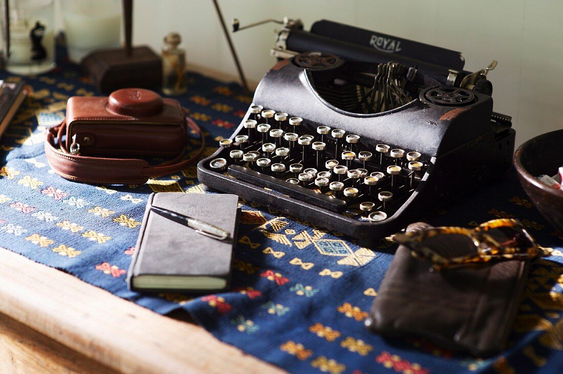 Vintage typewriter, sunglasses and notebook on wooden table with folklore blanket