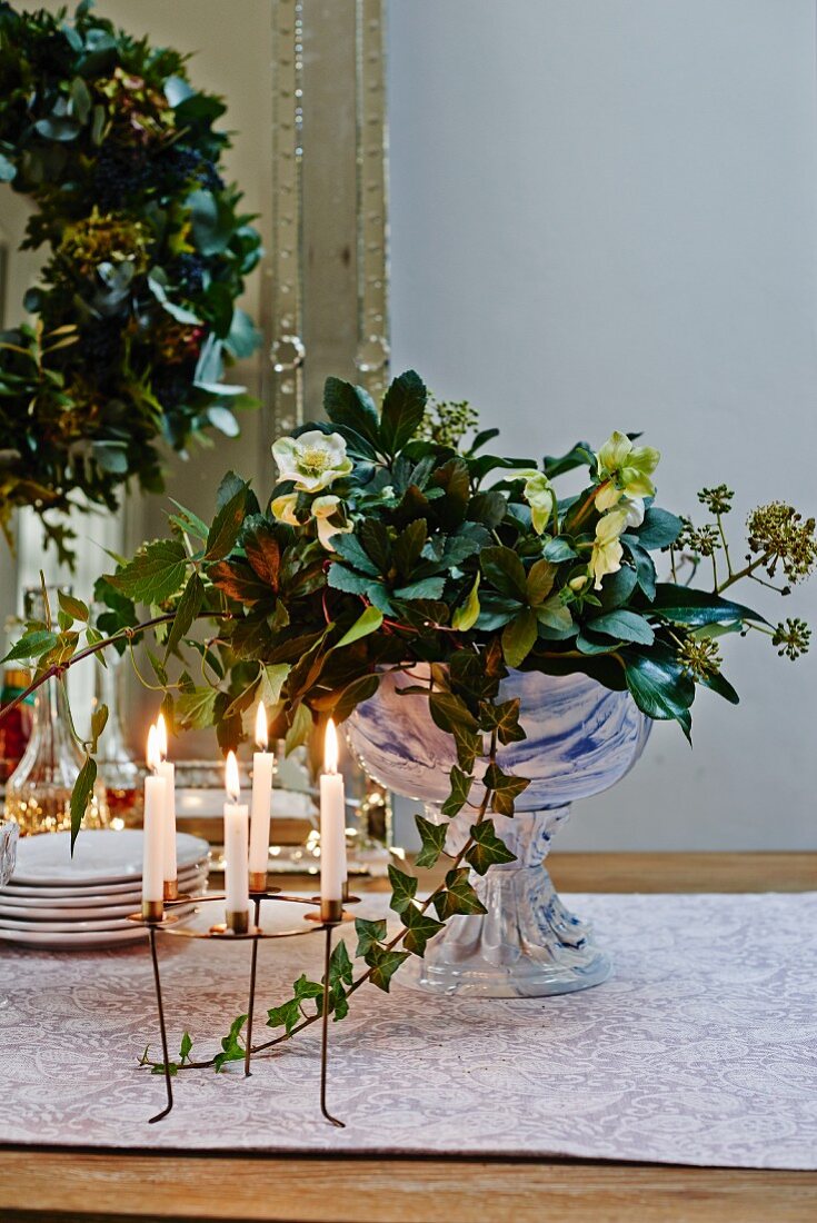Festive arrangement of hellebores in glass goblet dish and wreath-shaped candelabra on dresser