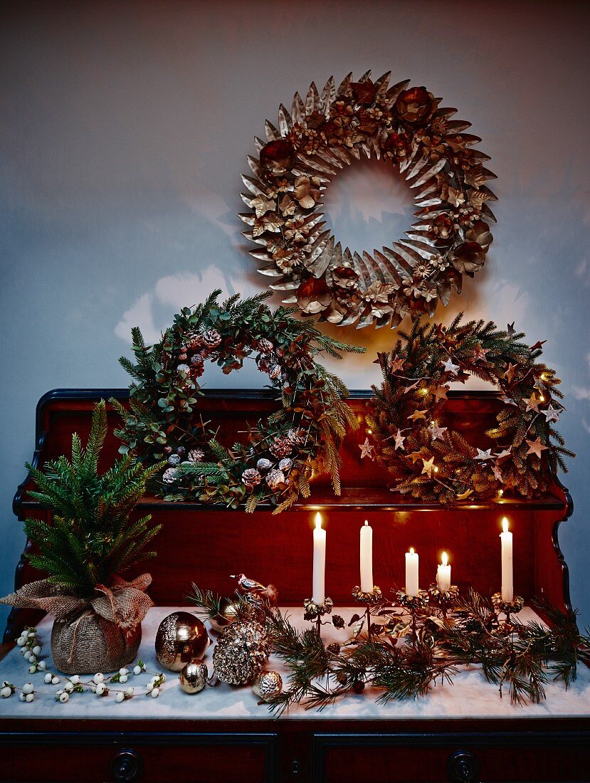 Verschiedene, kunstvoll gebundene Blätterkränze, Kerzen und Weihnachtsschmuck auf Kommode mit Aufsatz