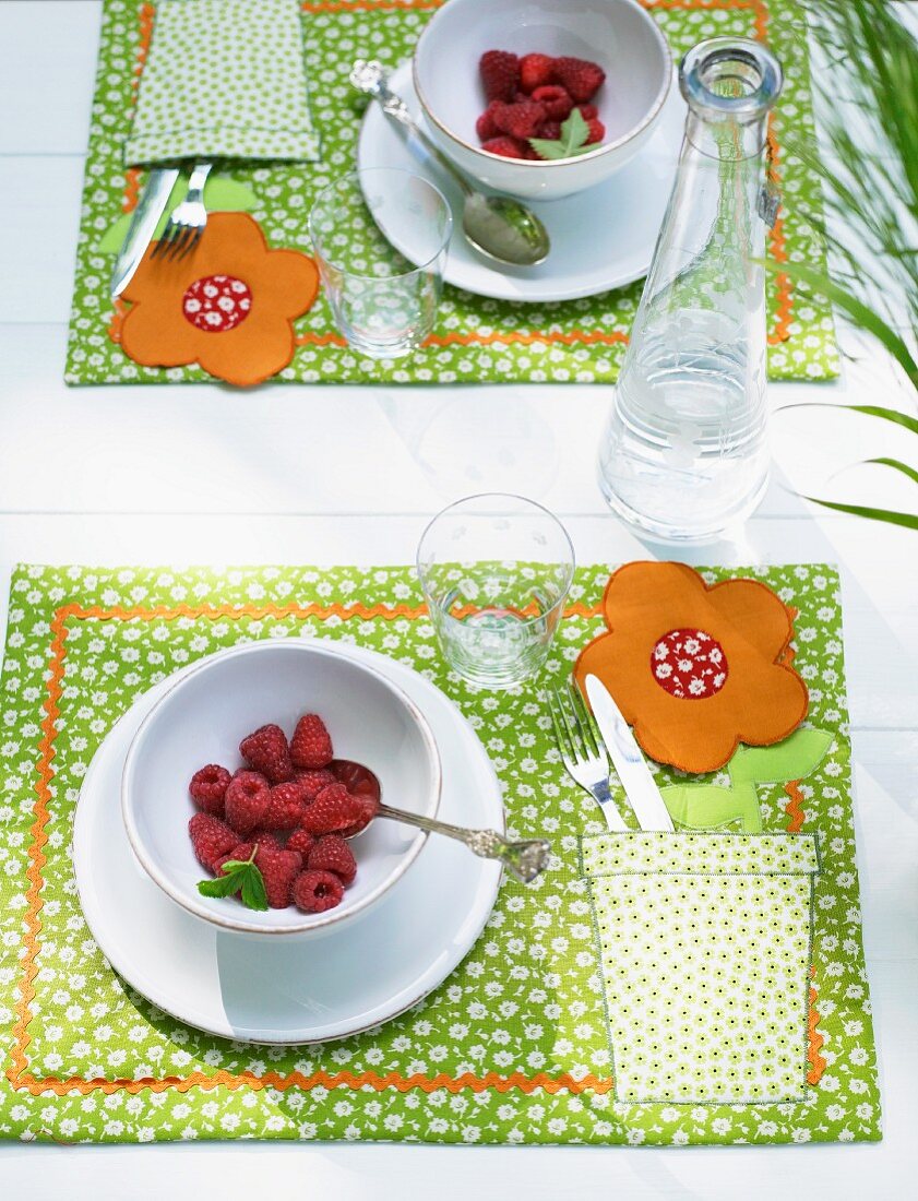 A place setting with raspberries and a homemade placemat with a floral pattern