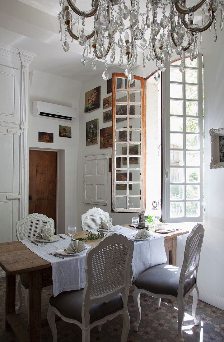 Rococo chairs around set table below open window and chandelier with glass pendants