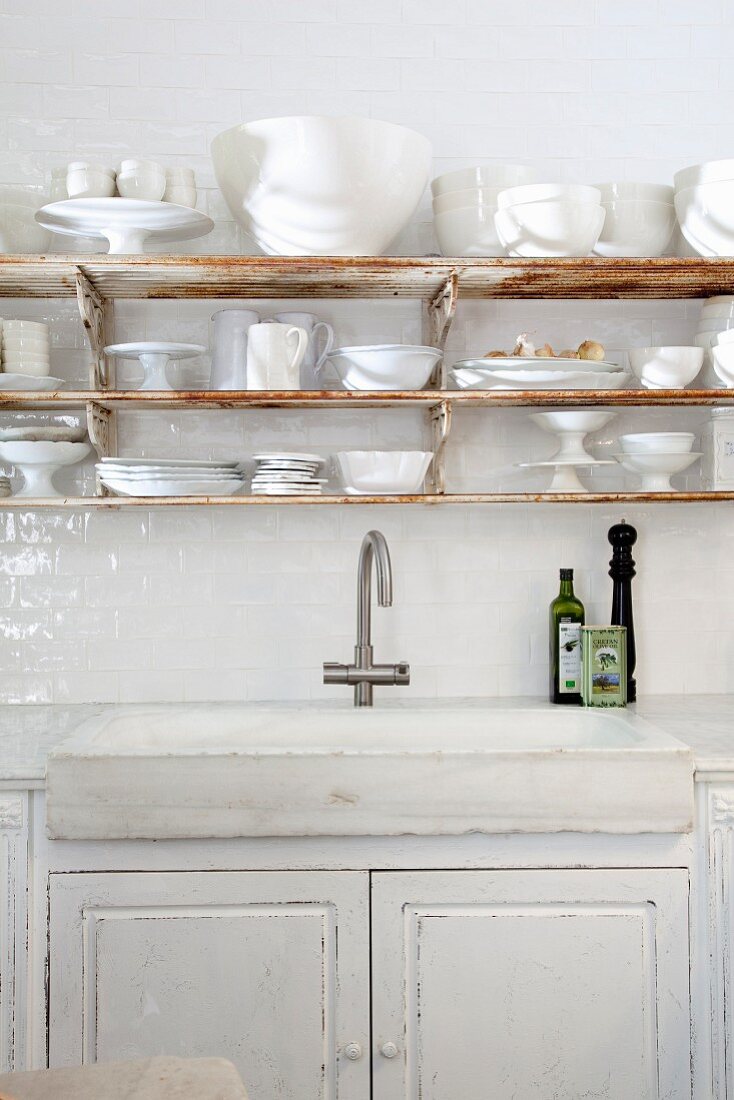 Küchenzeile mit rustikalem Spülbecken in Unterschrank, oberhalb weisses Geschirr auf rostiger Ablage
