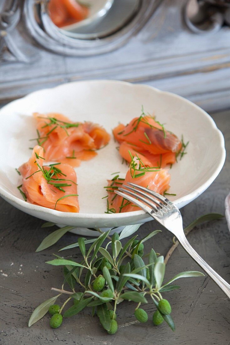 Salmon with dill in white bowl next to olive sprig