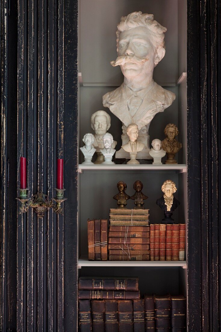 Detail of cupboard with various busts and antiquarian books behind glass door