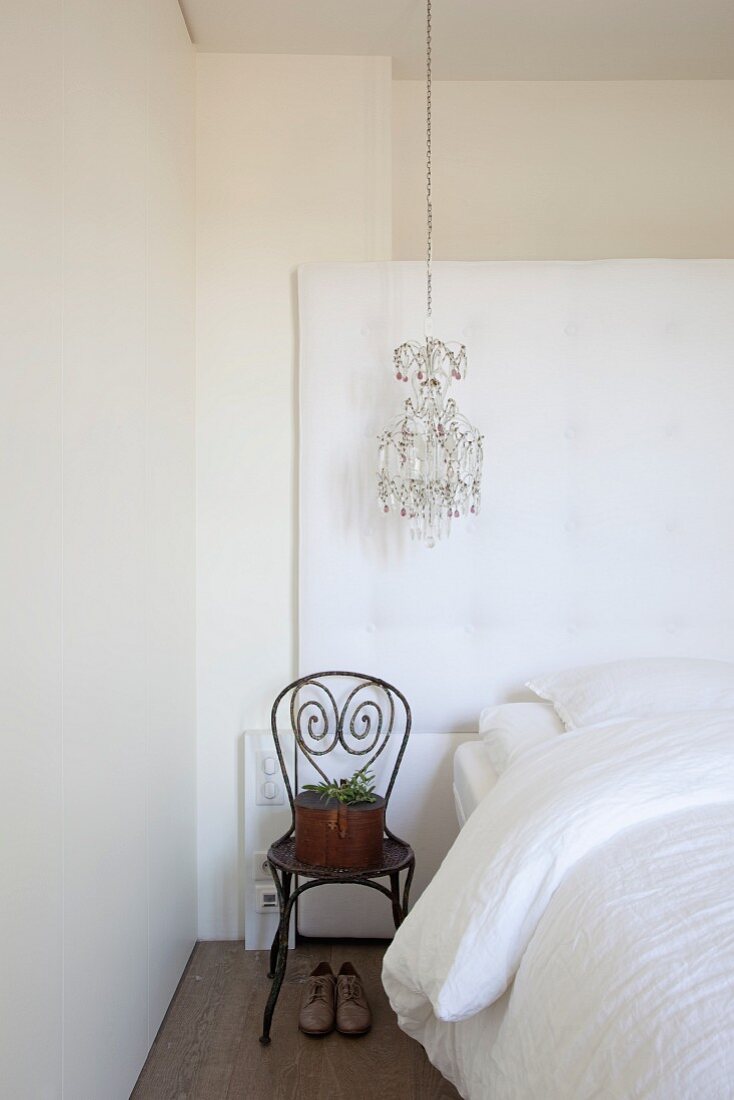 Potted plant on Thonet chair next to bed with white bed linen below chandelier