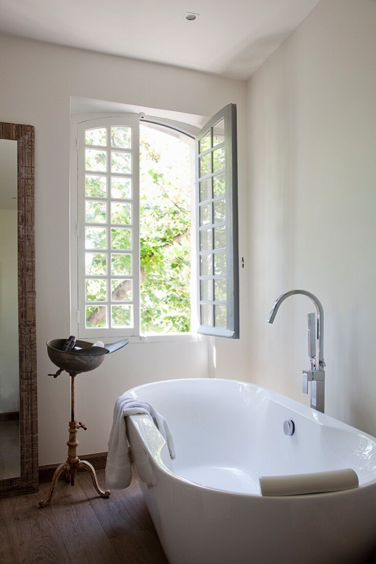 Free-standing bathtub with floor-mounted taps below open window