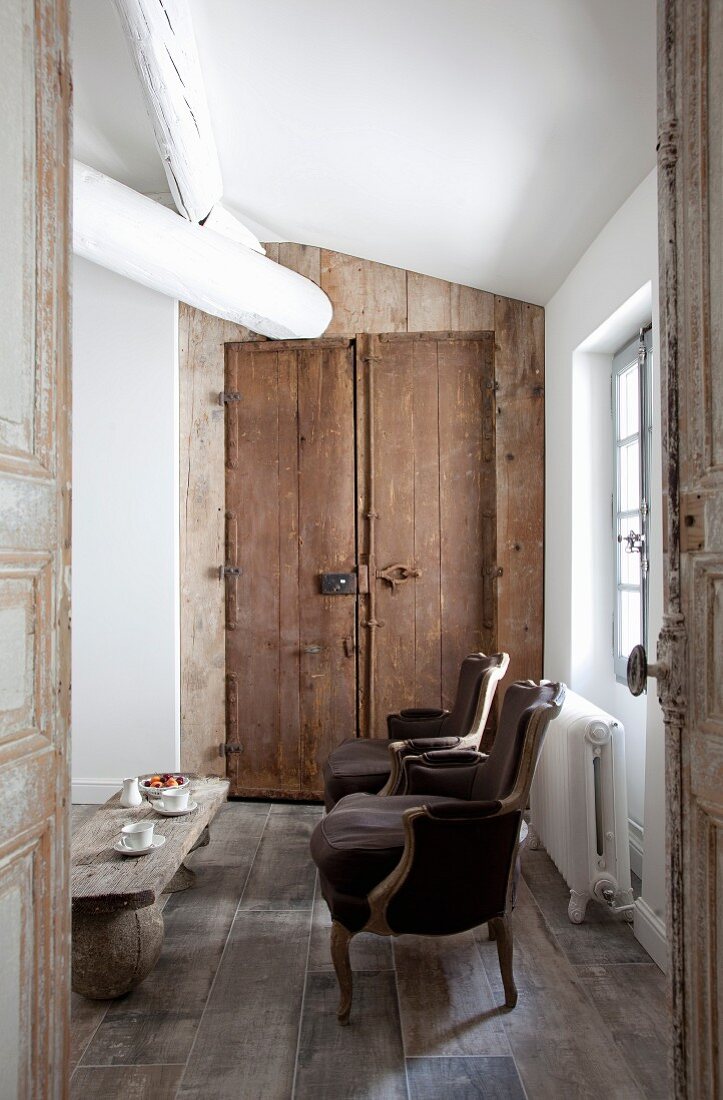 View through open door of Rococo-style antique armchair and rustic wooden door in background
