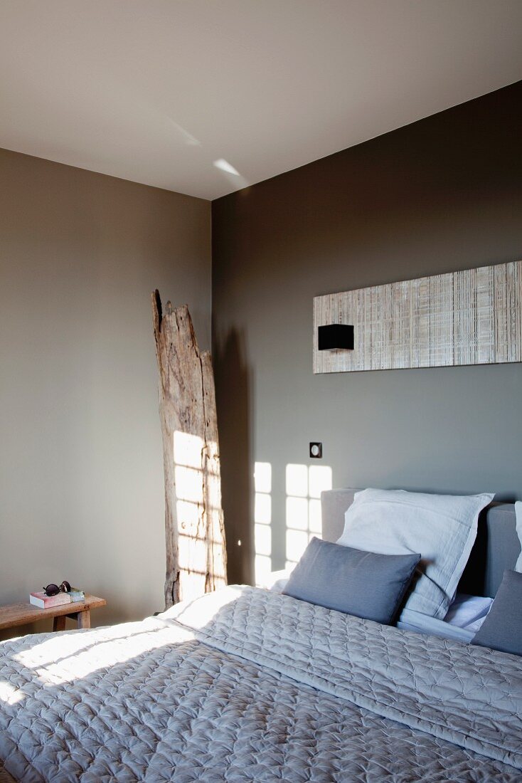 Schlafzimmer mit grau getönten Wänden, auf Doppelbett gestepptes Plaid
