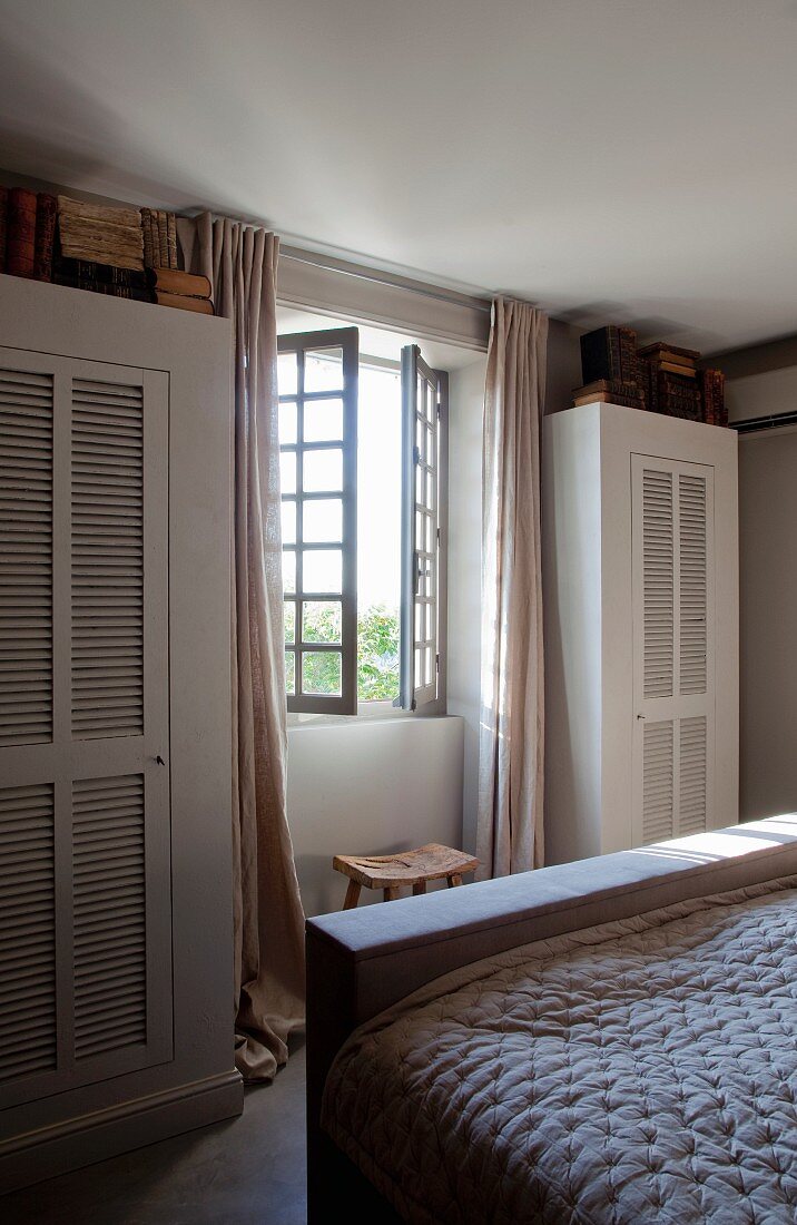 Wardrobes with louver doors flanking lattice window in bedroom