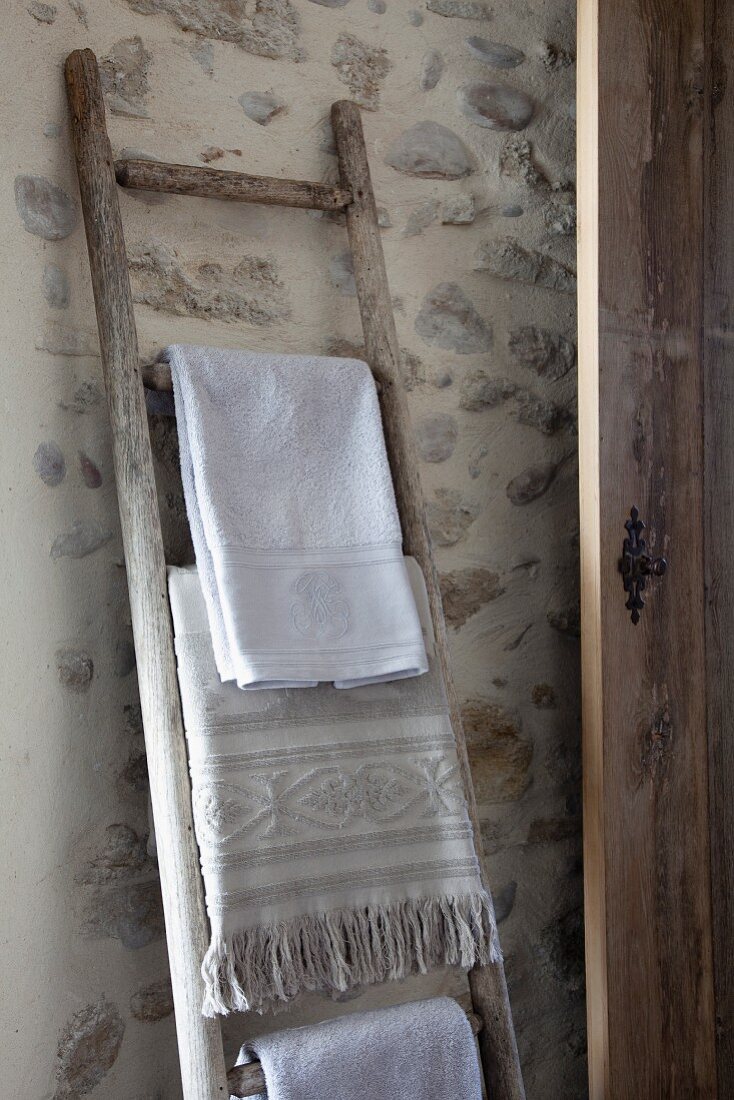 Old wooden ladder used as towel rack leaning against stone wall