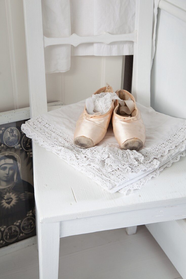 Vintage ballet shoes on lace cloth on white-painted kitchen chair
