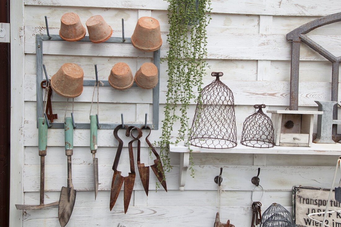 Garden tools and plant pots hung on white-painted wooden panel